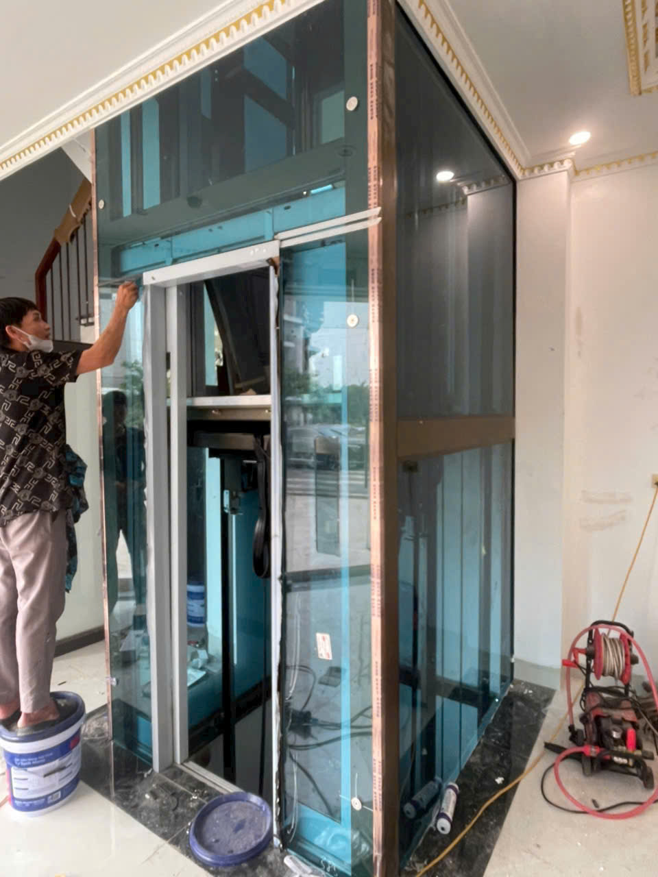 Lắp đặt thang máy kính gia đình trong nhà, kỹ thuật viên đang hoàn thiện khung và cửa thang máy